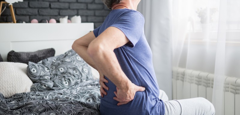 homme assis sur un lit, qui a des douleurs en bas du dos